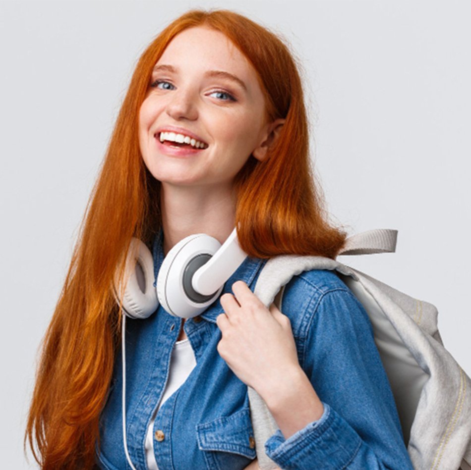college-life-modern-lifestyle-education-concept-cheerful-good-looking-redhead-female-student-with-foxy-long-hair-wearing-headphones-neck-backpack-smiling-camera